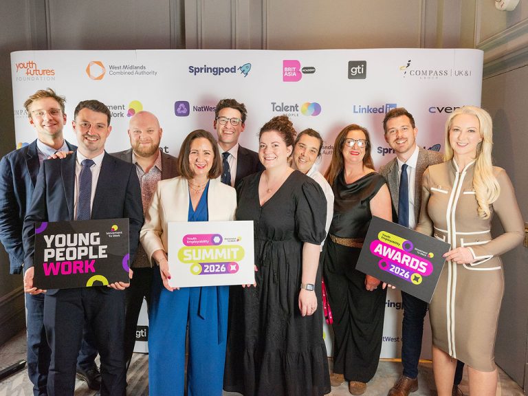The Movement to Work team line up in front of a banner with the event sponsor logos on.